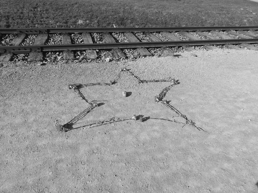 Vor einem Bahngleis ist aus Nelken ein Stern auf eine Sand-Schotterfläche gelegt. In der Mitte des Sterns befindet sich ein länglich-runder Stein mit der Aufschrift 10.4.2015